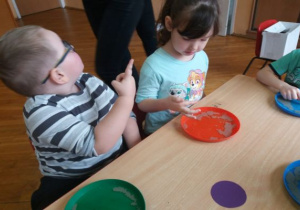 dzieci siedzą przy stolikach przy kolorowych talerzach